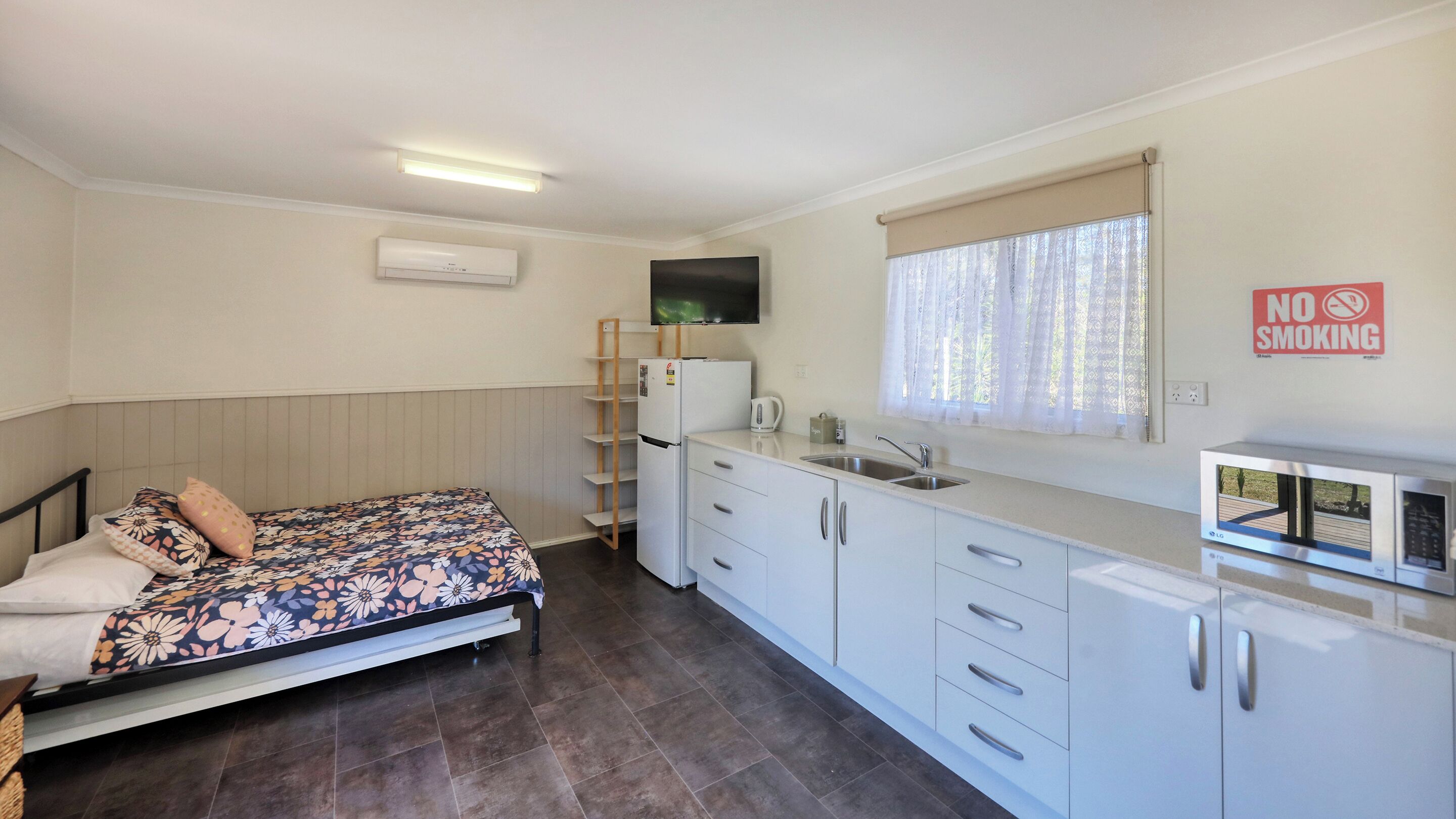 A compact room with a bed, a kitchenette, a TV, and a 'No Smoking' sign.
