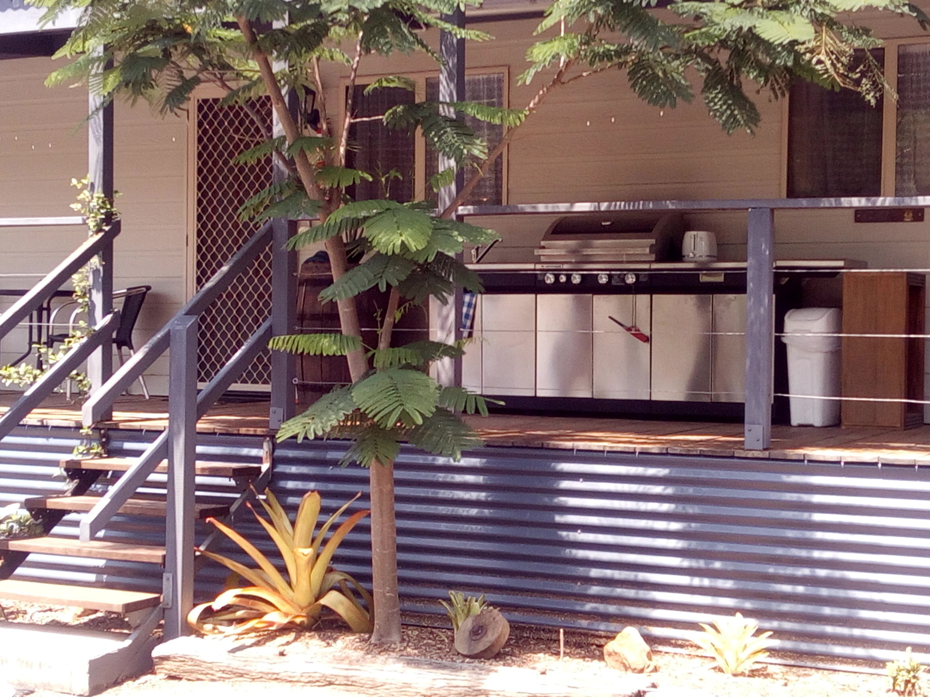 A building with a metal staircase, a small tree, and a kitchen area with cabinets and a stove.