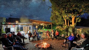 An outdoor gathering around a campfire with people seated on chairs and benches. - Silver Wattle Caravan Park (Hamilton Creek)