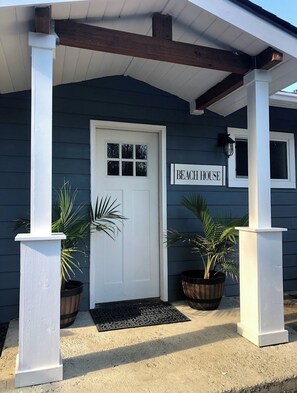 Een donkerblauwe woning met een witte deur en een bordje met de tekst 'BEACH HOUSE'.