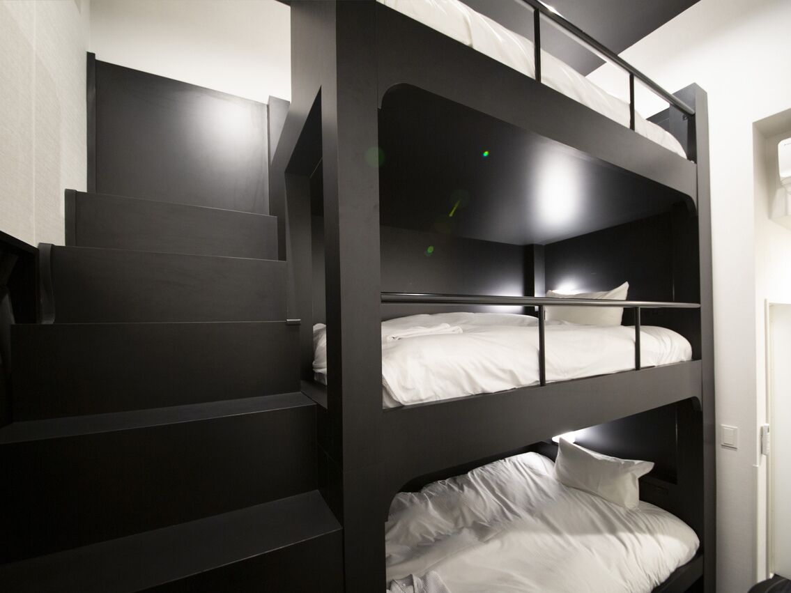 A bunk bed with a staircase leading up to it, a white door, and a light switch on the wall.