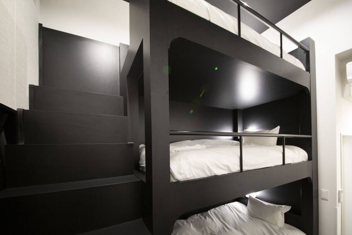 A bunk bed with a staircase leading up to it, a white door, and a light switch on the wall.