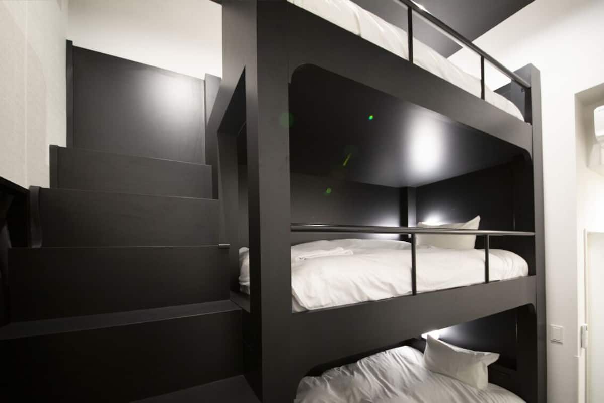 Una cama litera con una escalera que lleva hasta arriba, una puerta blanca y un interruptor de luz en la pared.