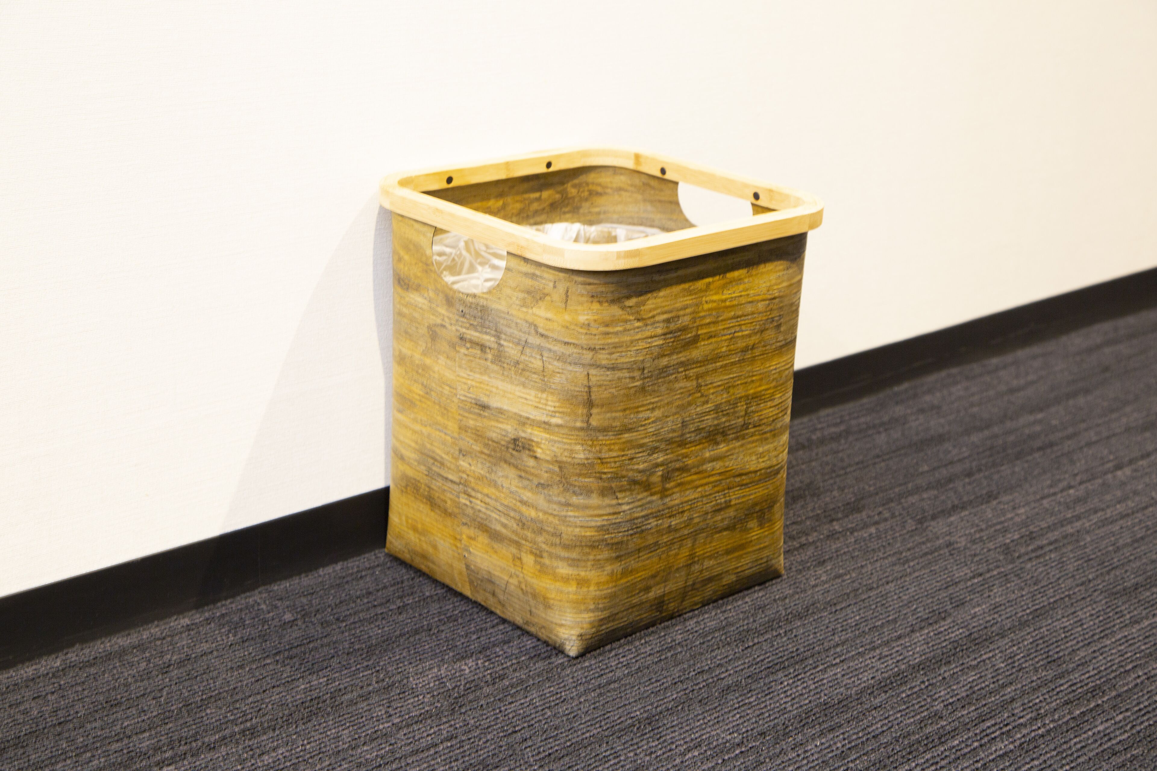 A wooden trash bin with a transparent lid on a carpeted floor.