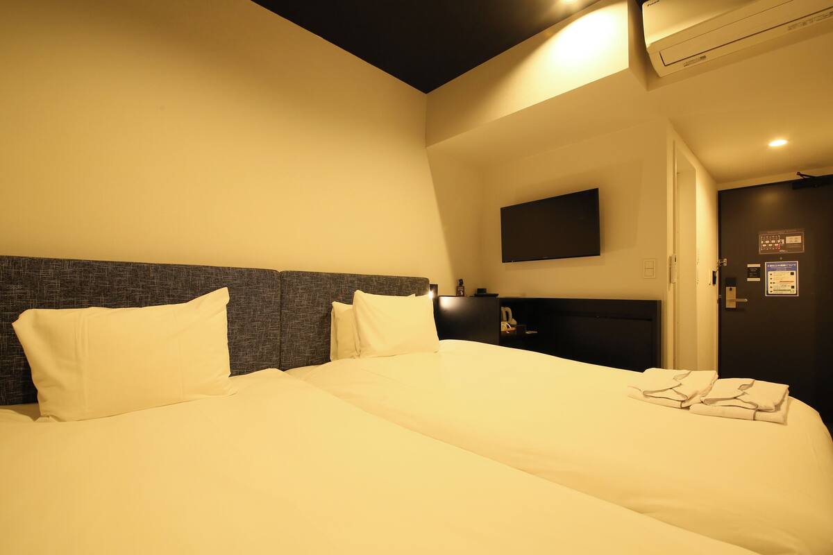 A hotel room with a large bed, a flat-screen TV mounted on the wall, and a door with a sign.