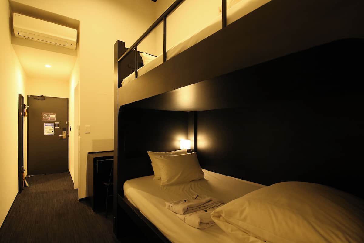 A hotel room with a bunk bed, a bedside table, and a wall-mounted air conditioner.