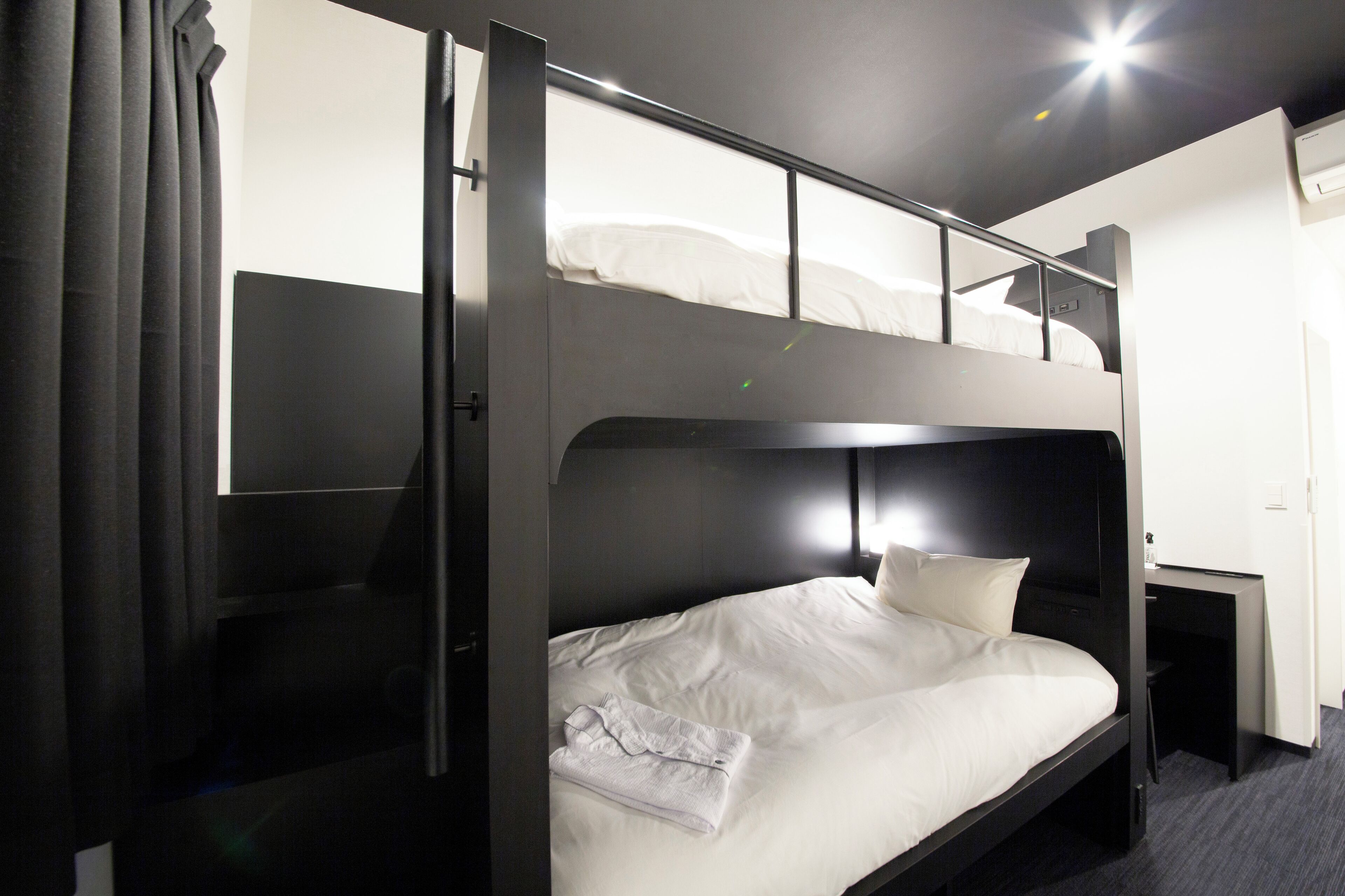 Cama litera con escritorio y silla, ventana con cortinas y aire acondicionado instalado en la pared.