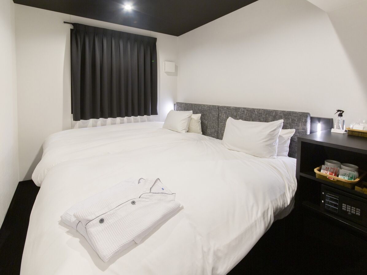 A hotel room with a large bed, a bedside table, a nightstand, and a window with curtains.