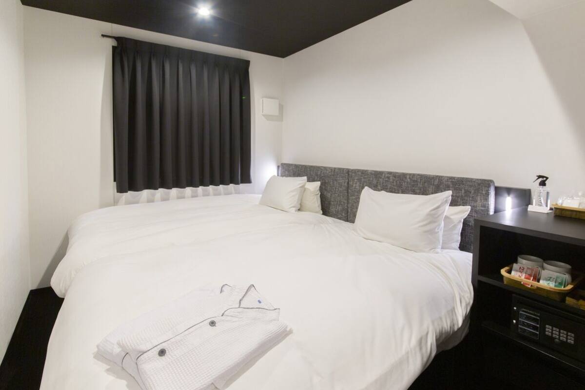 A hotel room with a large bed, a bedside table, a nightstand, and a window with curtains.