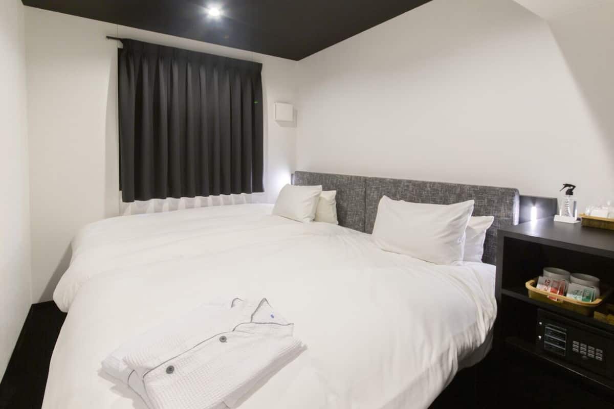 Una habitación de hotel con una cama grande, una mesita de noche y un ventanal con cortinas.