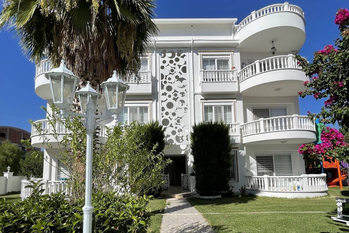 A multi-story building with balconies, a patterned walkway, and lush greenery.