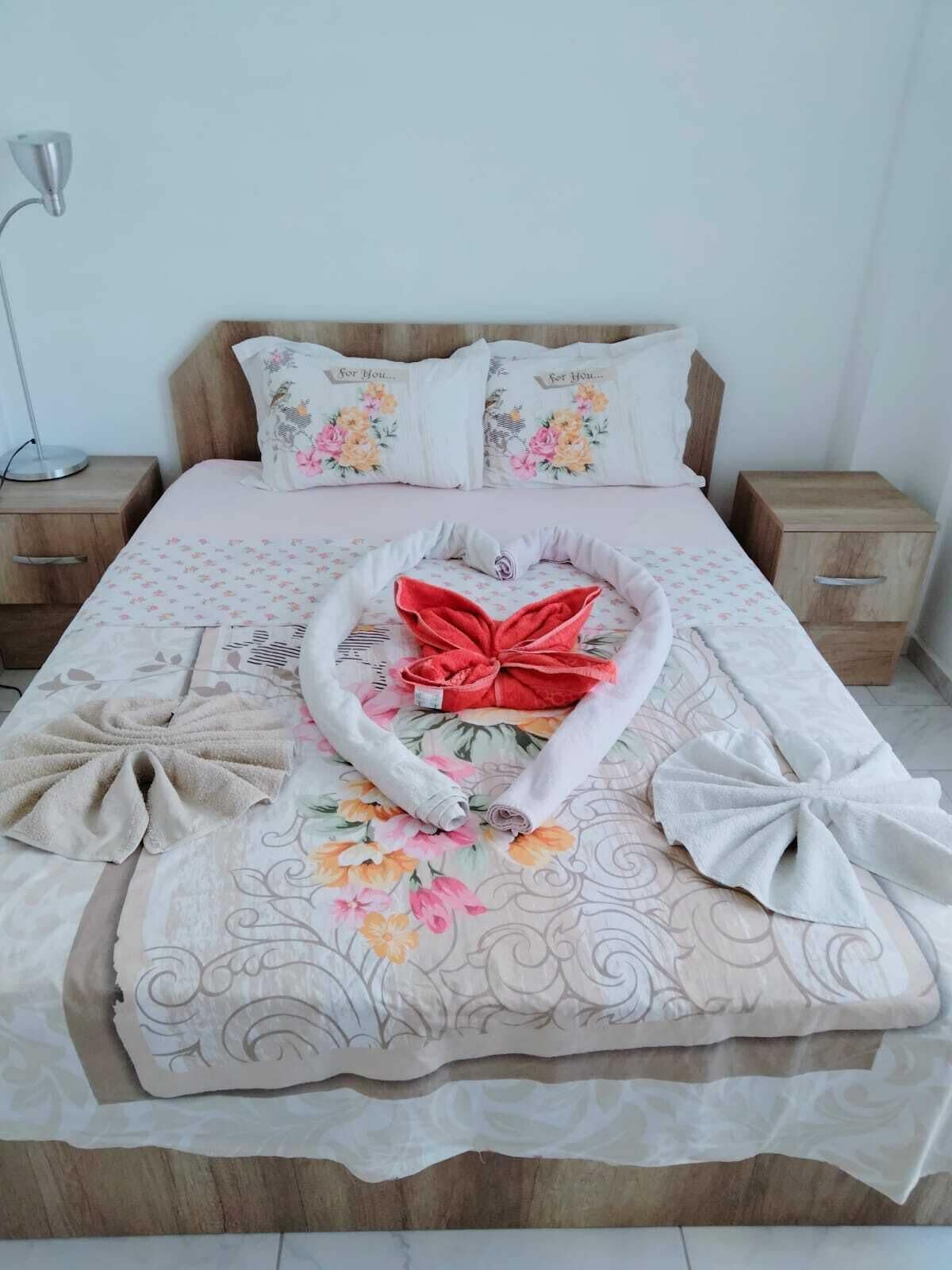 Ein ordentlich bezogenes Bett mit Blumenmuster, einem roten Band und aufgerollten Handtüchern.
