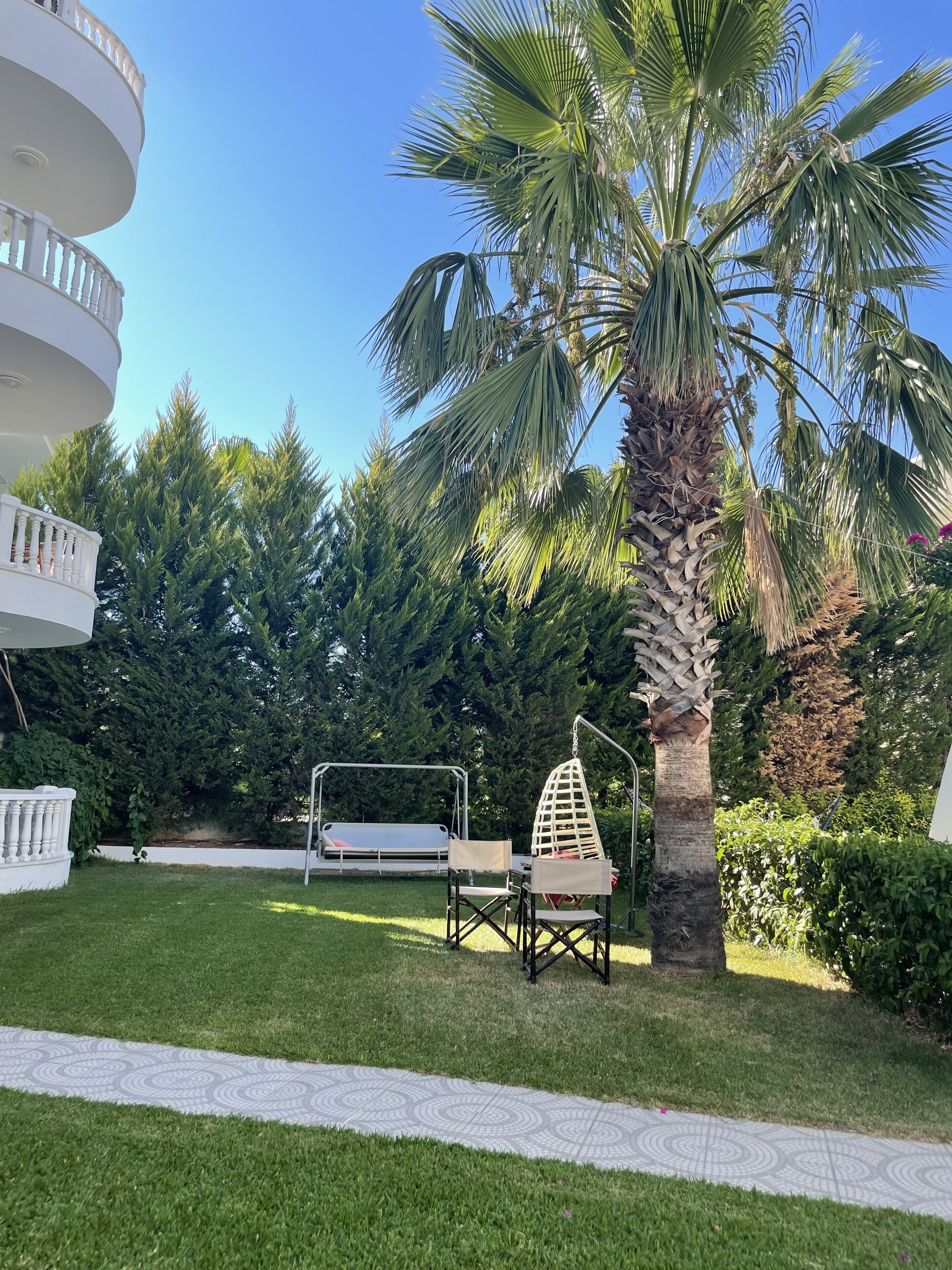 Un'area esterna ben curata con una palma, un'altalena e una zona relax con mobili bianchi.