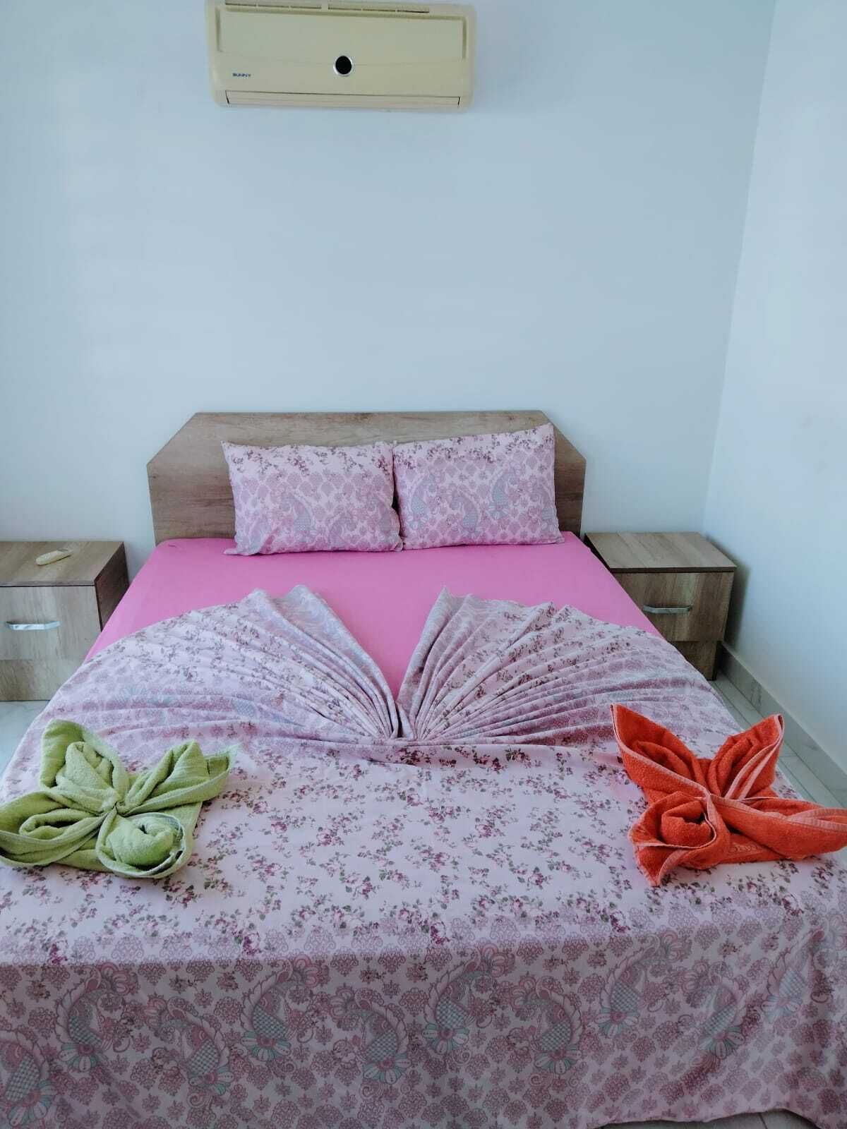 A bed with a pink bedspread, two pillows, and a decorative book arrangement on the bed.