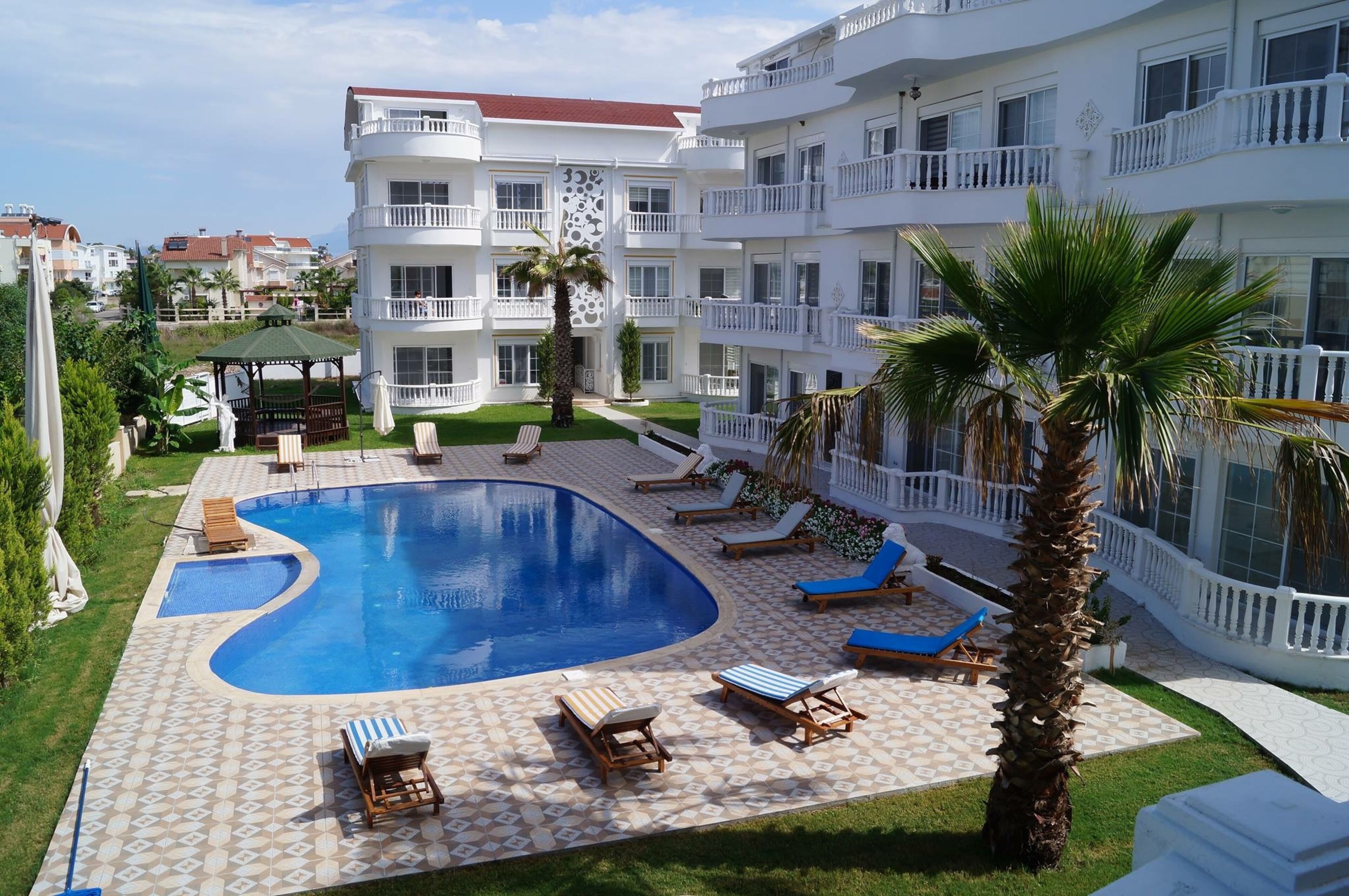 A hotel with a swimming pool, lounge chairs, and a well-maintained garden.