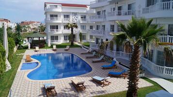 A hotel with a swimming pool, lounge chairs, and a well-maintained garden.