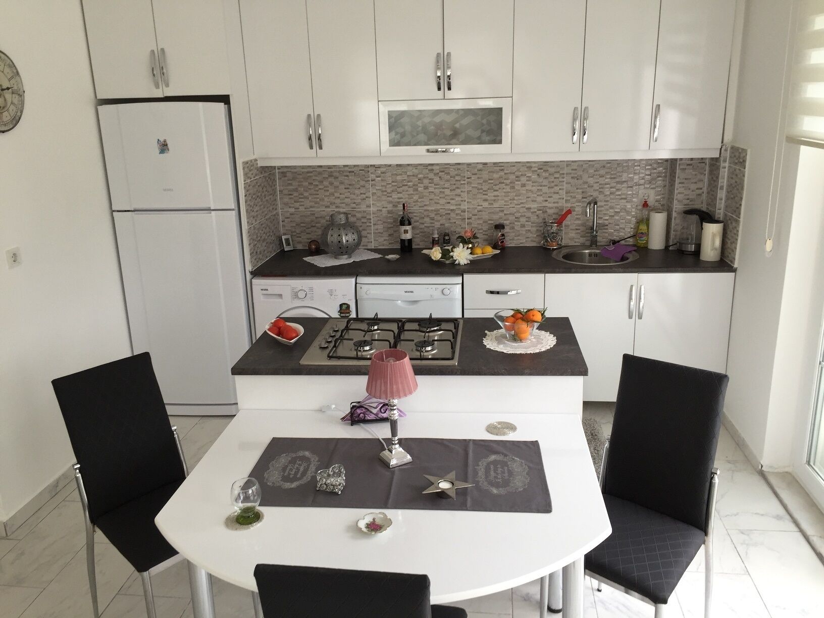 Una cocina moderna con armarios blancos, estufa a gas y microondas. Hay una mesa de comedor con sillas y un tapete decorativo.