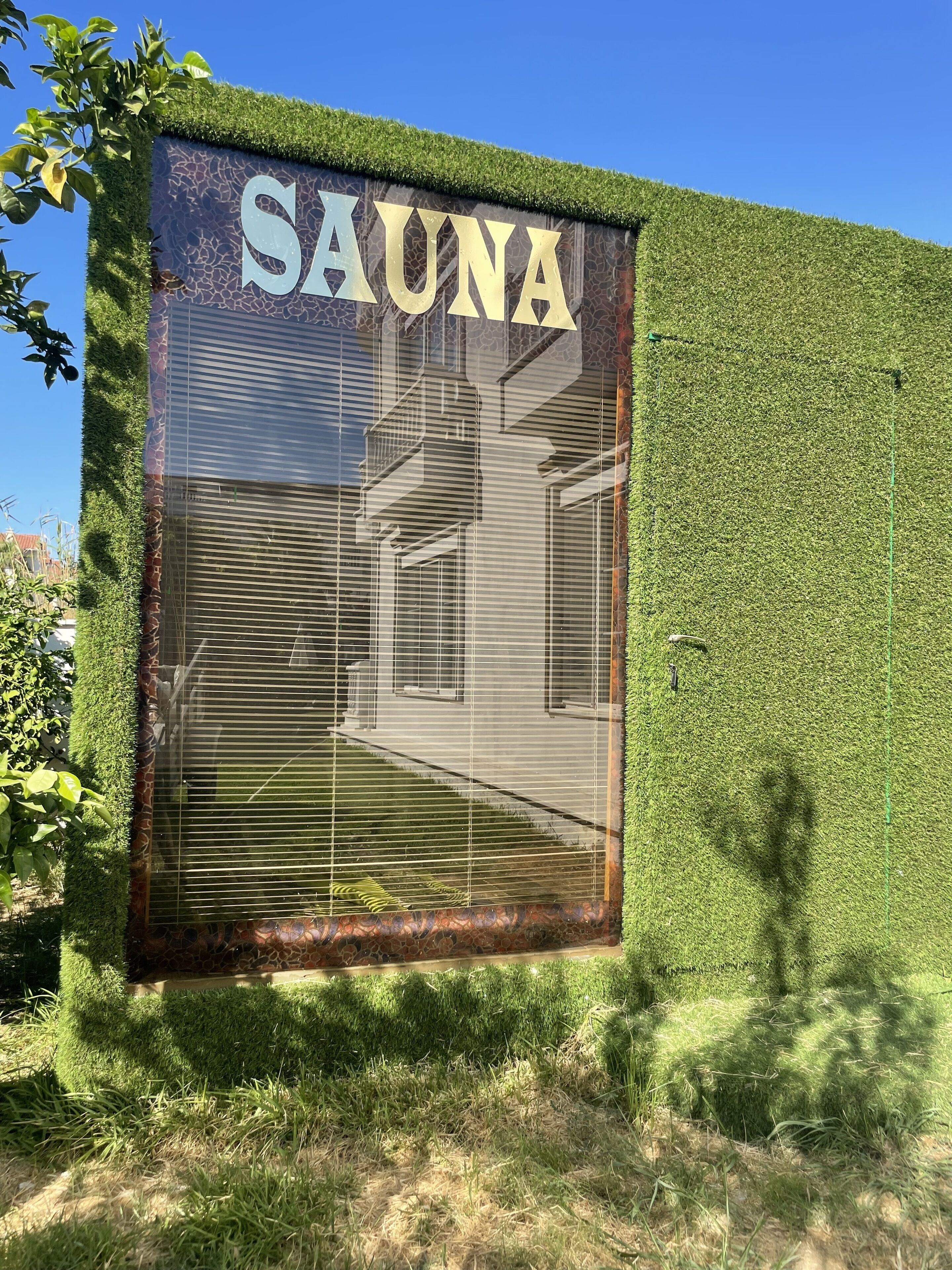 Um sinal com a palavra 'SAUNA' numa parede com textura que lembra relva verde.