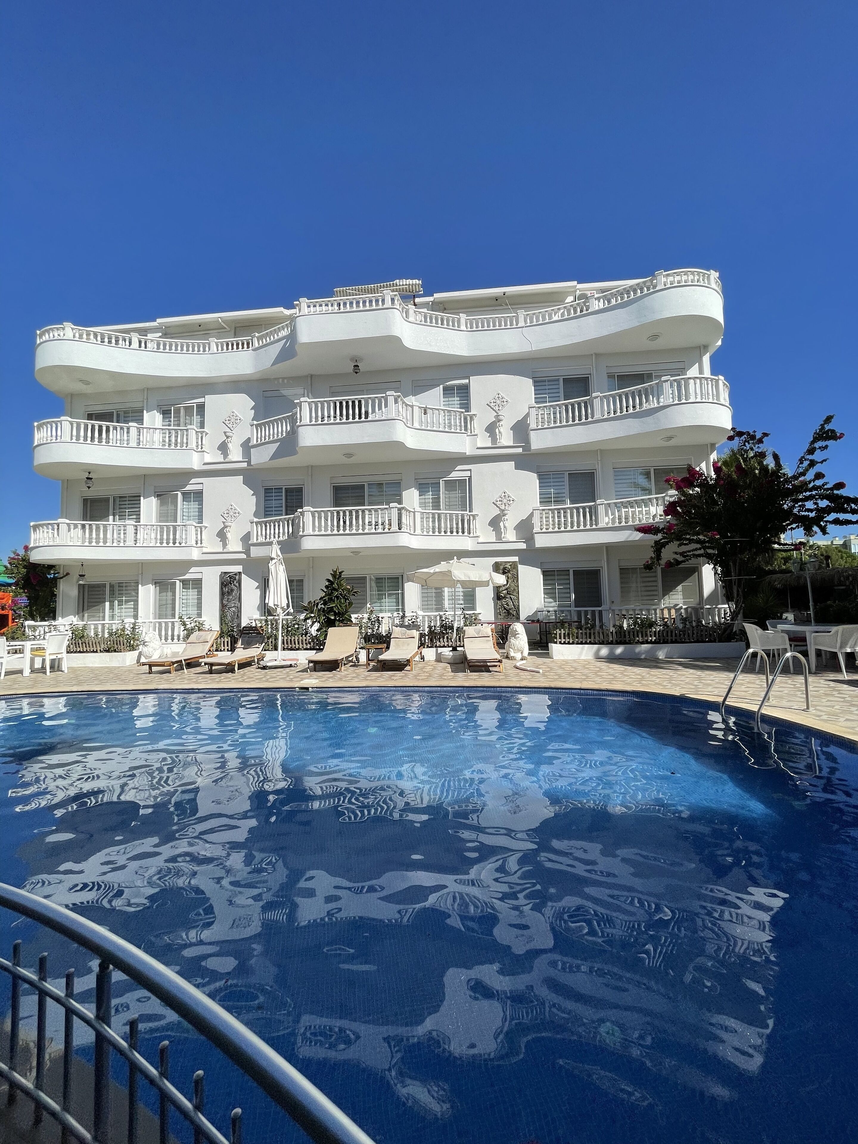 A multi-story hotel with a swimming pool, outdoor seating, and a well-maintained garden.