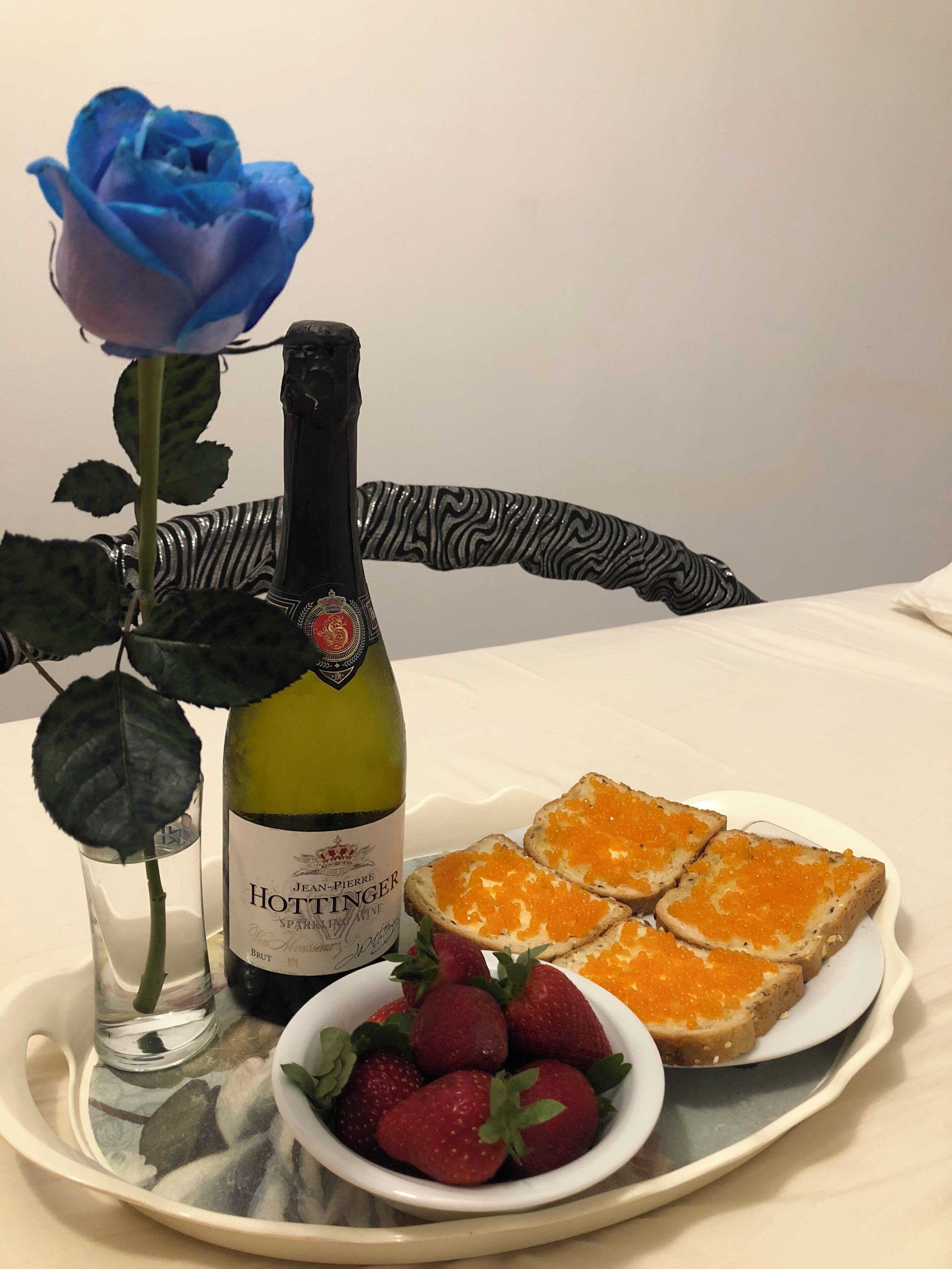 A bottle of Jean-Pierre Hottinger sparkling wine, a blue rose, strawberries, and orange caviar on toast.