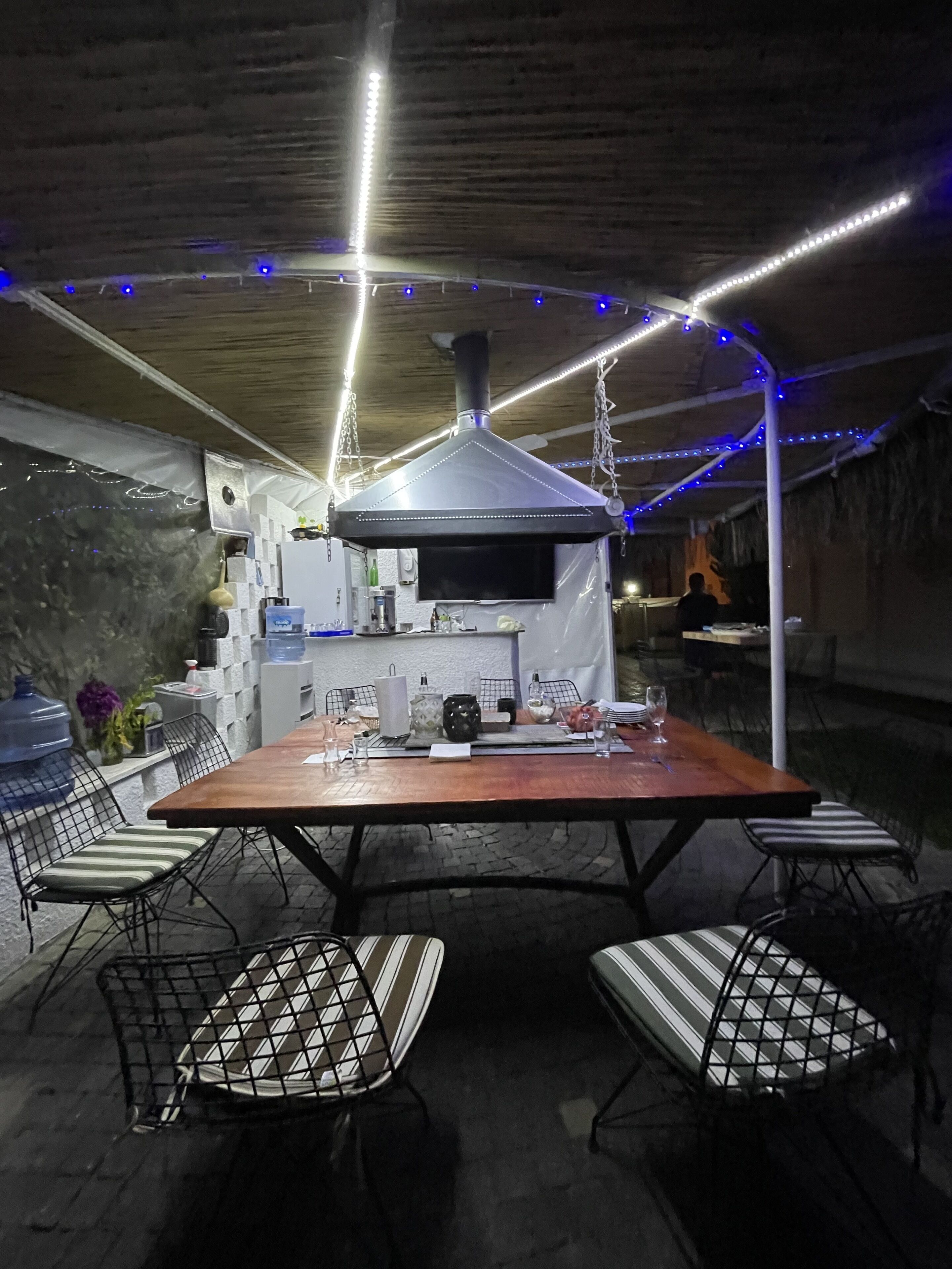 Un patio al aire libre con una mesa de ladrillo, sillas de metal y un horno de pizza.