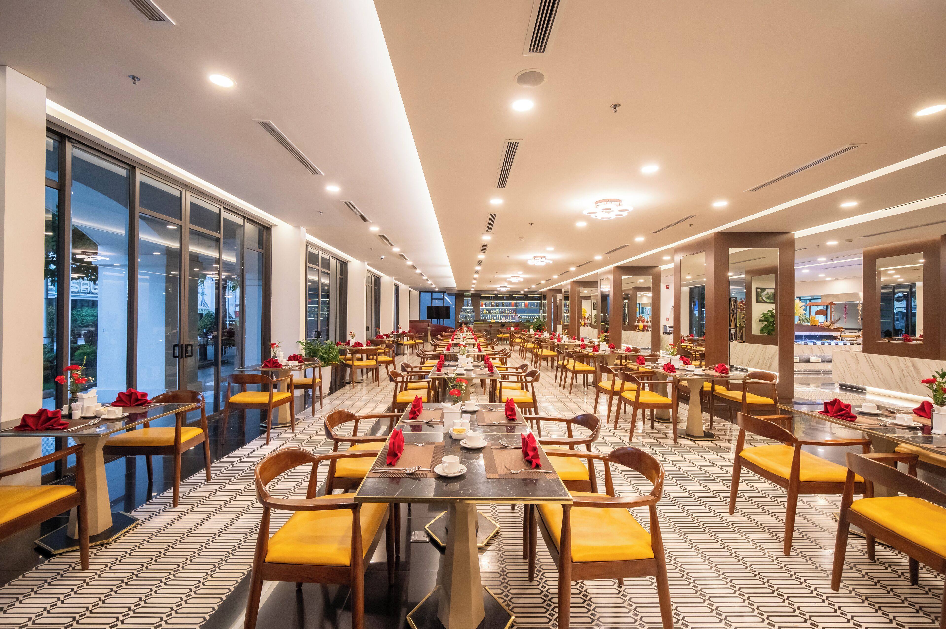 A spacious dining area with long tables, yellow chairs, and red napkins.