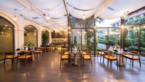 A restaurant with multiple dining tables and chairs, large windows, and a view of greenery outside. - Senna Hue Hotel (Hue)