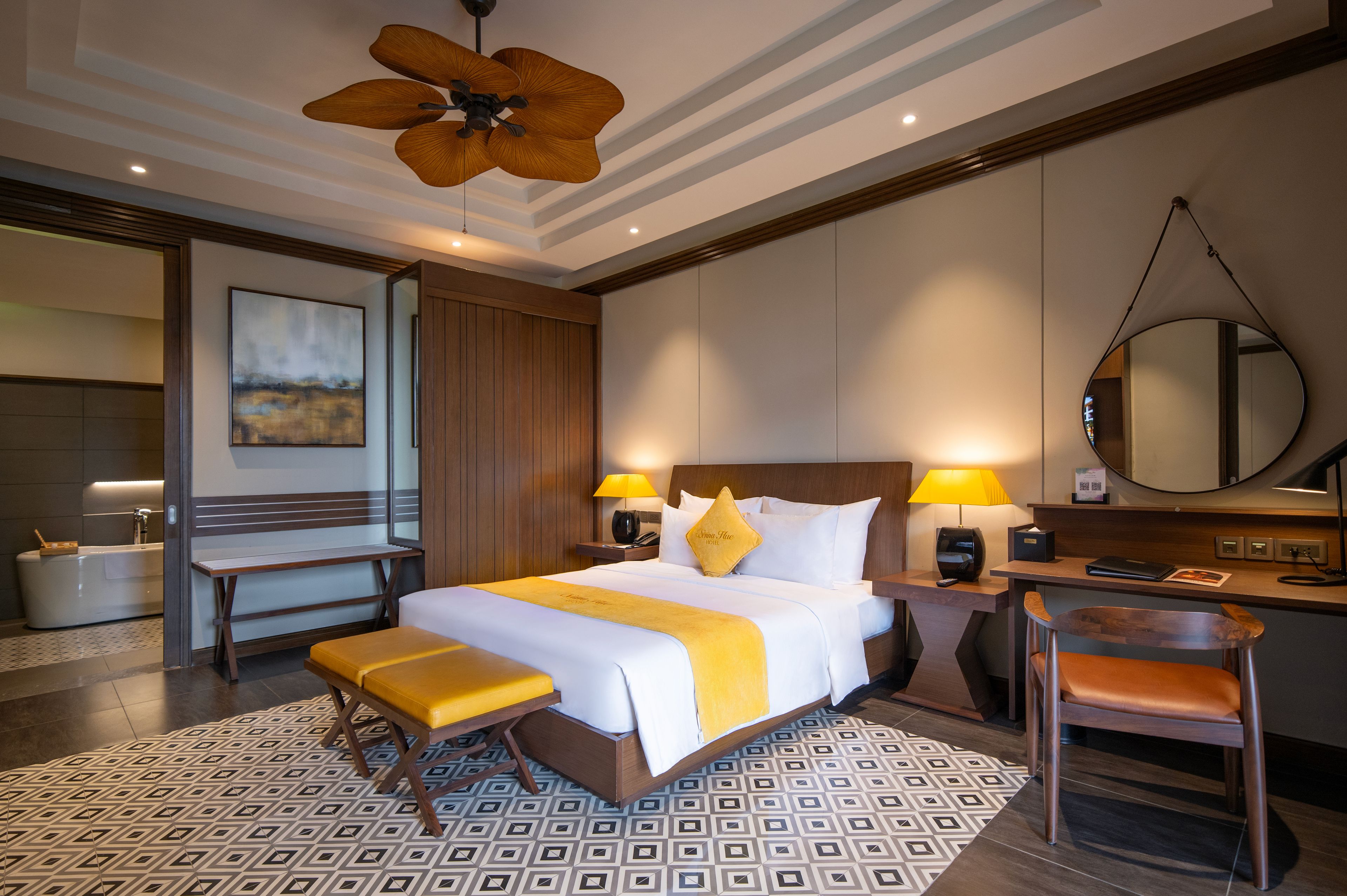 Ein Hotelzimmer mit einem großen Bett, Nachttischlampen, einem Schreibtisch, einem Sessel und einem Badezimmer mit einer Badewanne.