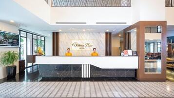 Ein Hotel-Rezeptionsbereich mit Marmor-Theke, zwei Rezeptionisten in gelben Uniformen und einem großen Schild über der Theke.