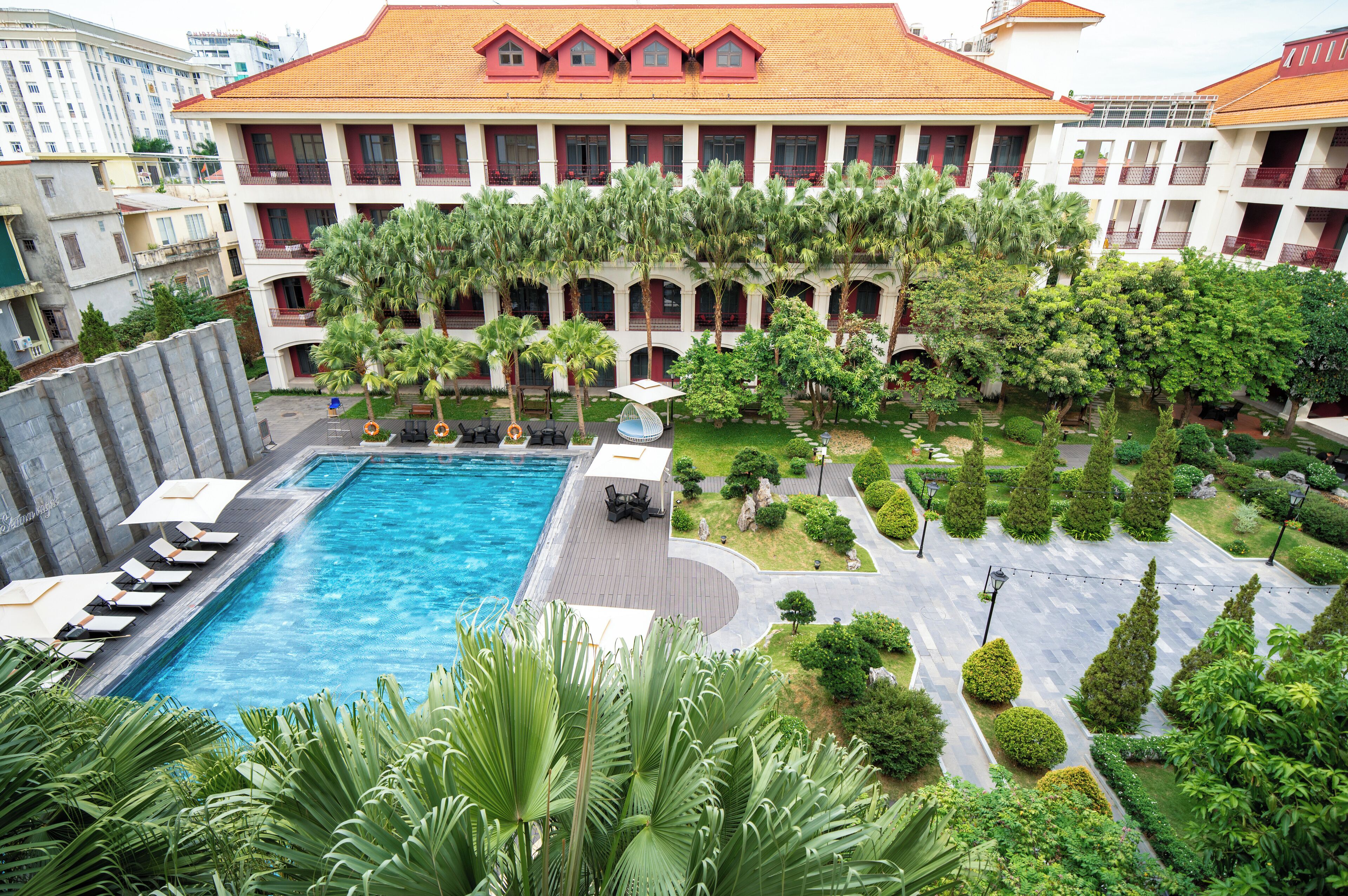 Ein Hotelinnenhof mit Swimmingpool, Palmen und einer überdachten Sitzgelegenheit.