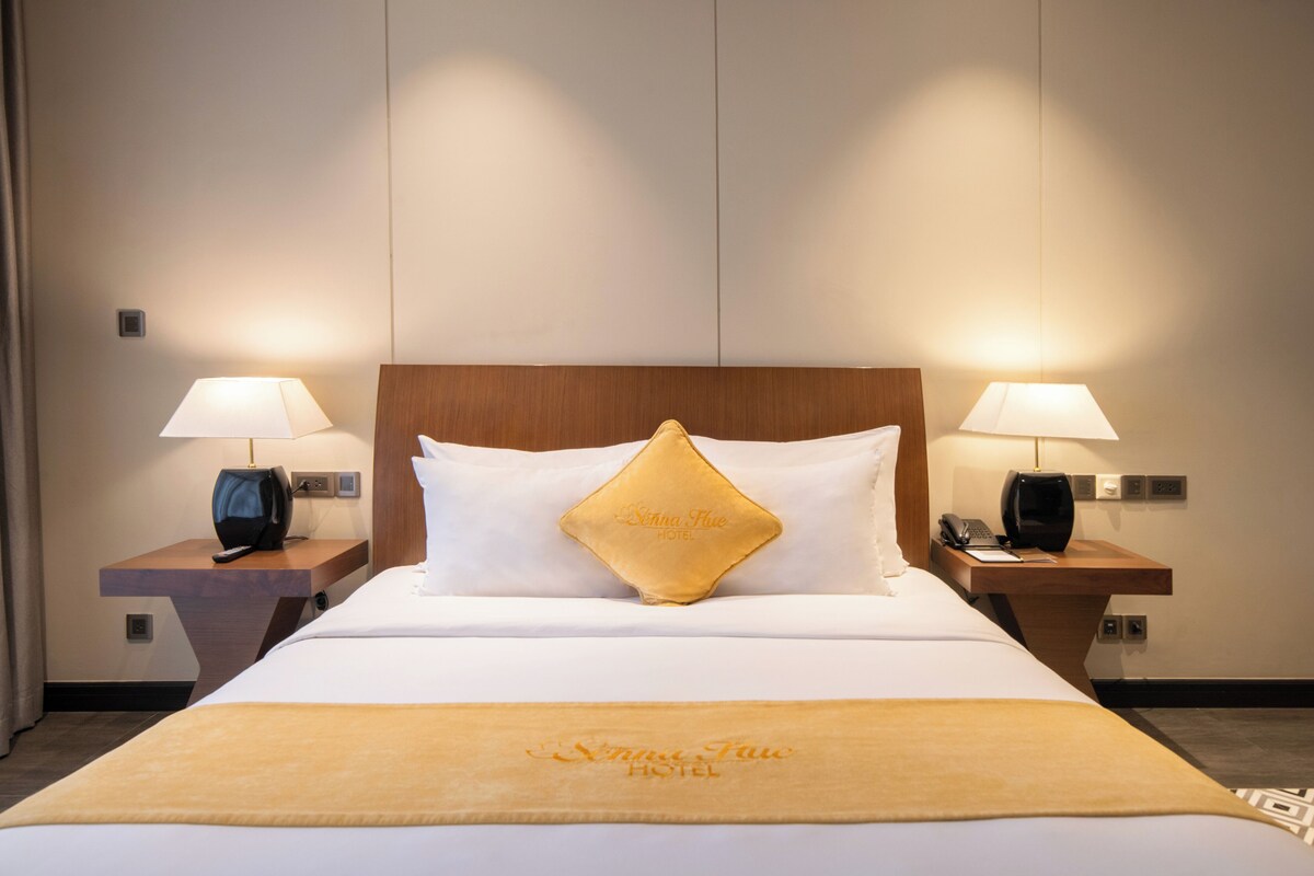 A hotel room with a large bed, two bedside tables, lamps, a telephone, and a decorative pillow.