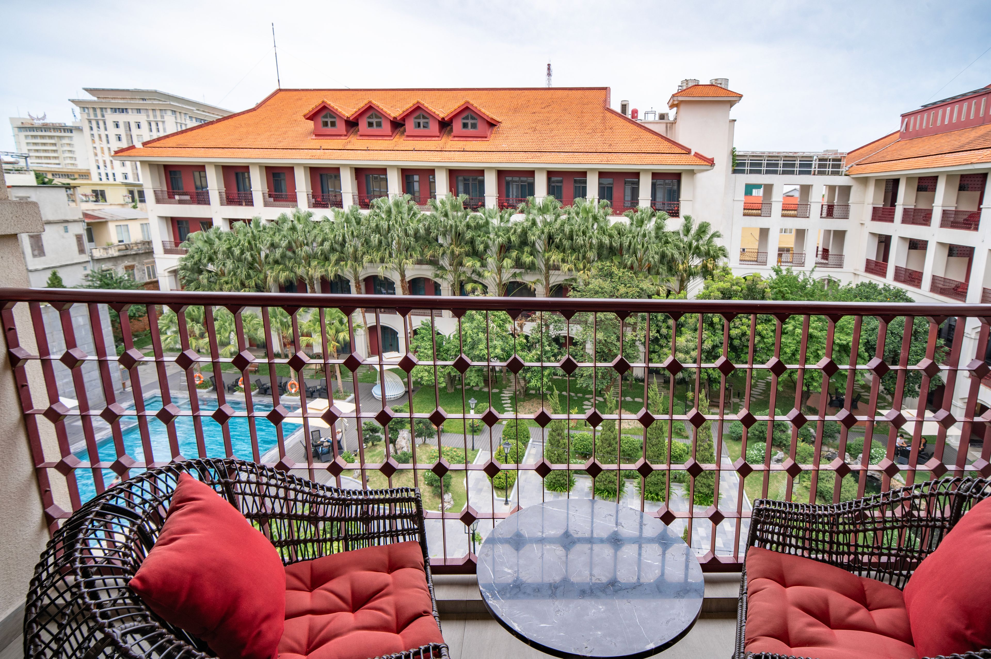 A balcony with wicker furniture and a view of a swimming pool and a building with red roofs.