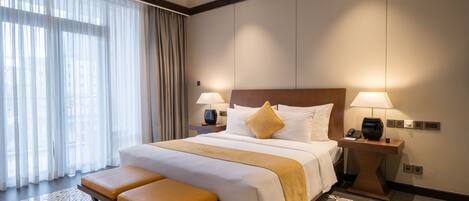 A hotel room with a large bed, two bedside tables, a bench, and a patterned floor.