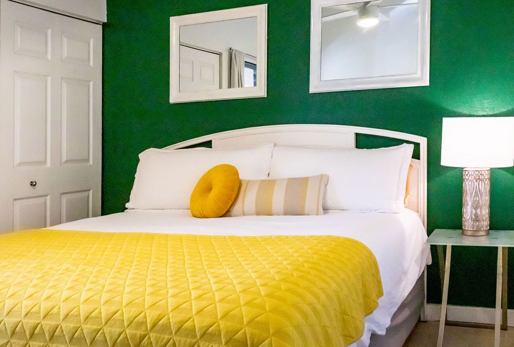A hotel room with a white bed, green walls, and a yellow bedspread.