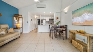 Un soggiorno moderno con un divano, un'area pranzo con sedie, una cucina con mobili bianchi e un quadro di grandi dimensioni appeso al muro.
