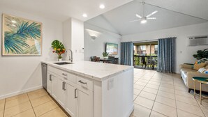 Eine moderne Küche mit Kochinsel, ein Essbereich mit Tisch und Stühlen sowie ein Wohnzimmer mit Sofa und Fernseher.