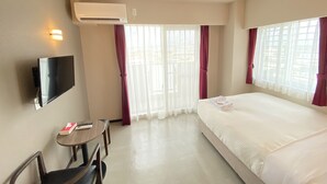 A hotel room with a bed, a desk with a chair, a TV mounted on the wall, and an air conditioning unit. - Popular Makiminato (Urasoe)