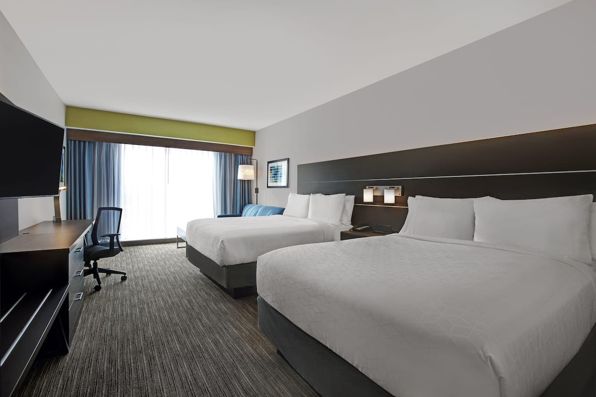 A hotel room with two beds, a desk, a chair, and a TV.