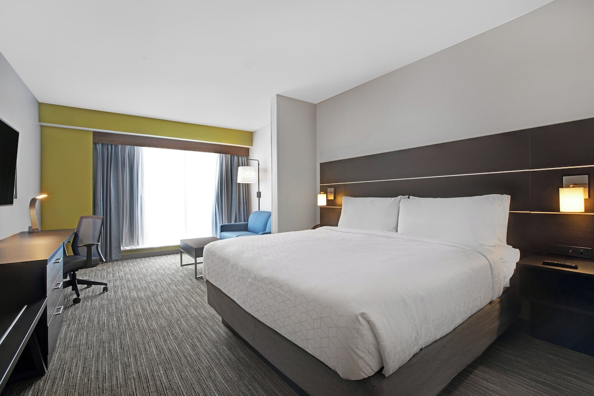 Een hotelkamer met een groot bed, een bureau, een stoel, een televisie en een raam met gordijnen.