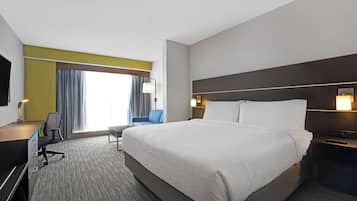 A hotel room with a large bed, a desk, a chair, a TV, and a window with curtains.