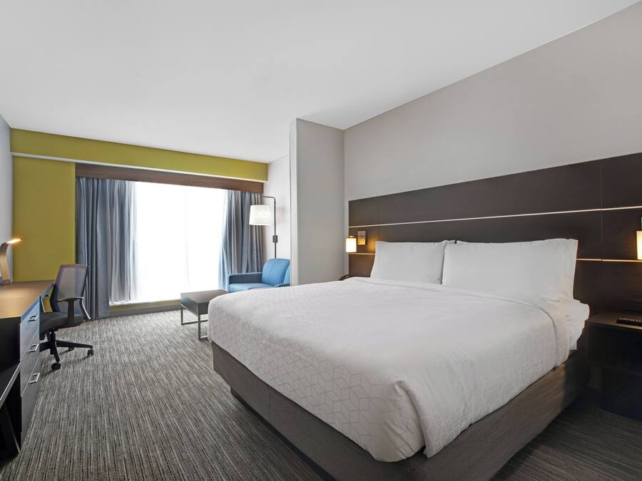 A hotel room with a large bed, a desk, a chair, a TV, and a window with curtains.