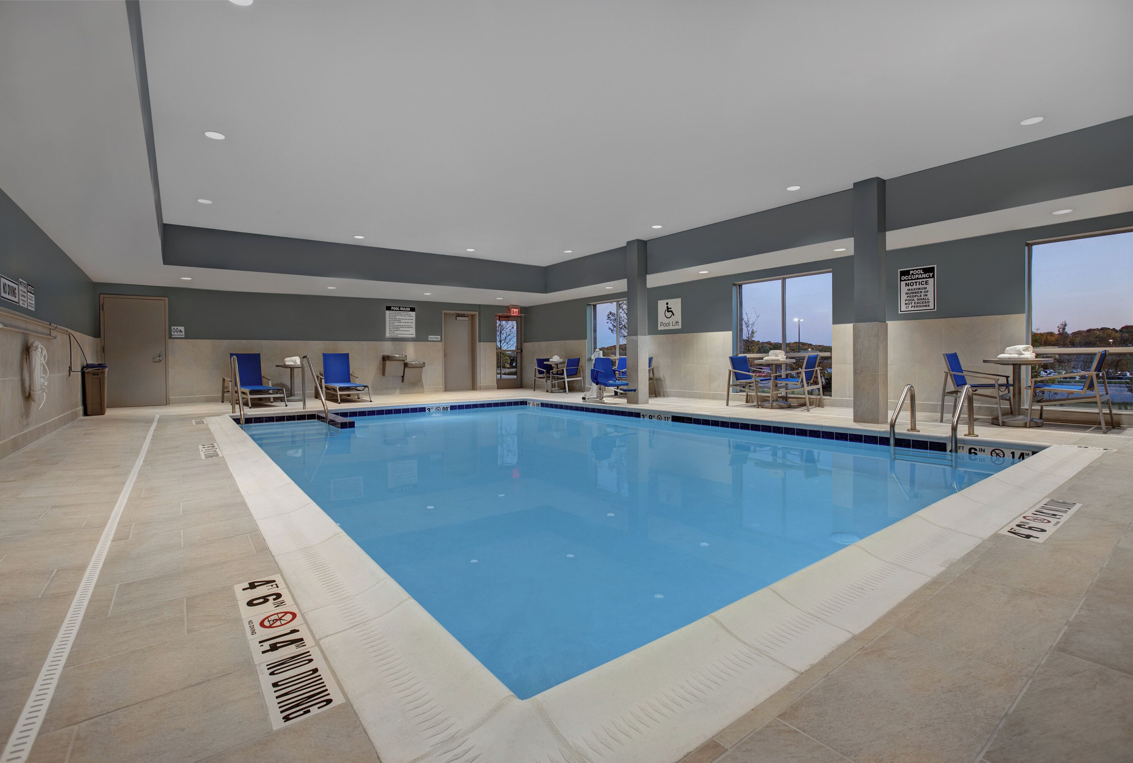 An indoor swimming pool with clear pool rules and a lifeguard chair.