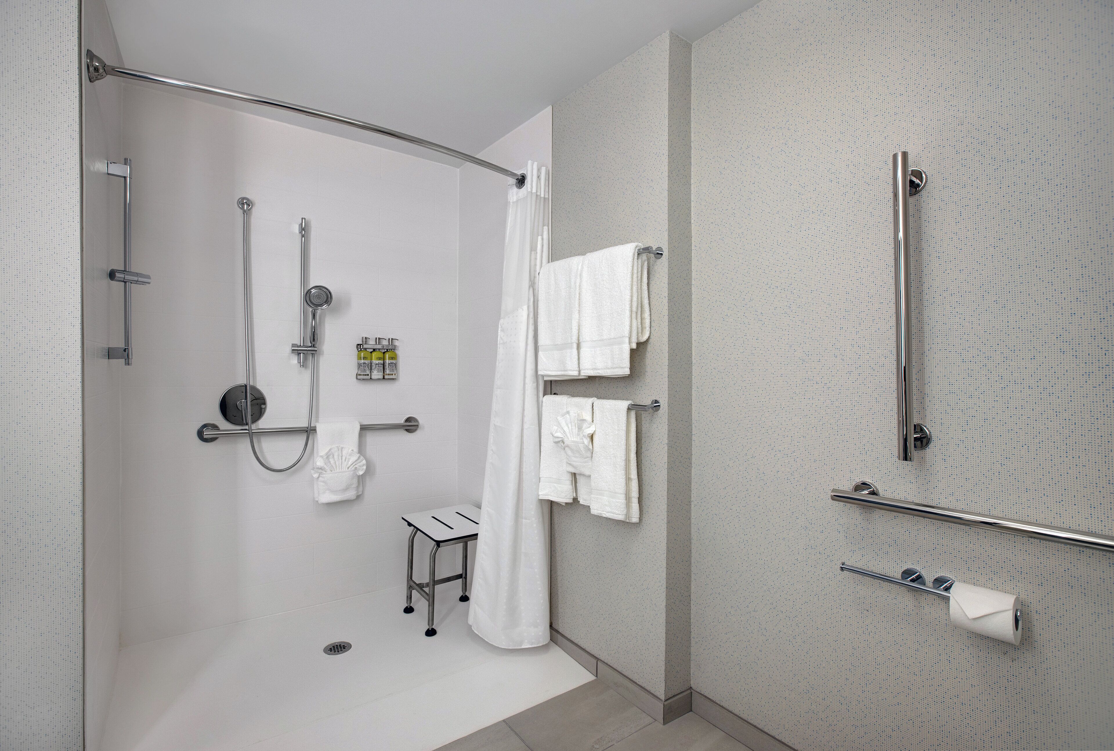 A modern bathroom with a walk-in shower, grab bars, a small stool, and a towel rack.