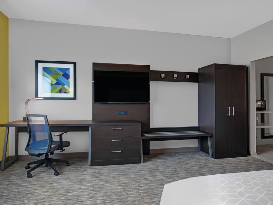 A hotel room with a desk, chair, television, wardrobe, and a bed.