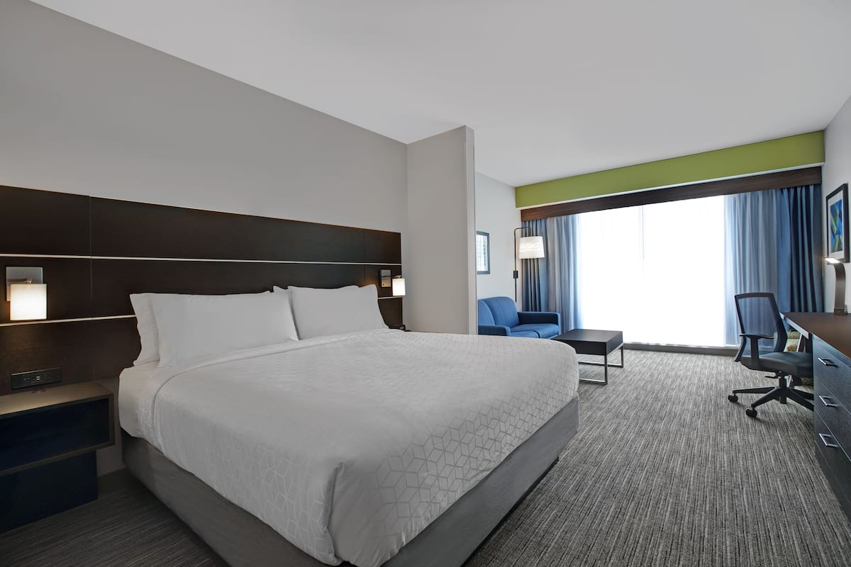 A hotel room with a large bed, a desk, a chair, and a window with curtains.
