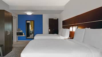 Une chambre d’hôtel avec deux lits, une armoire, un miroir et un petit coin salon avec une table et des chaises.