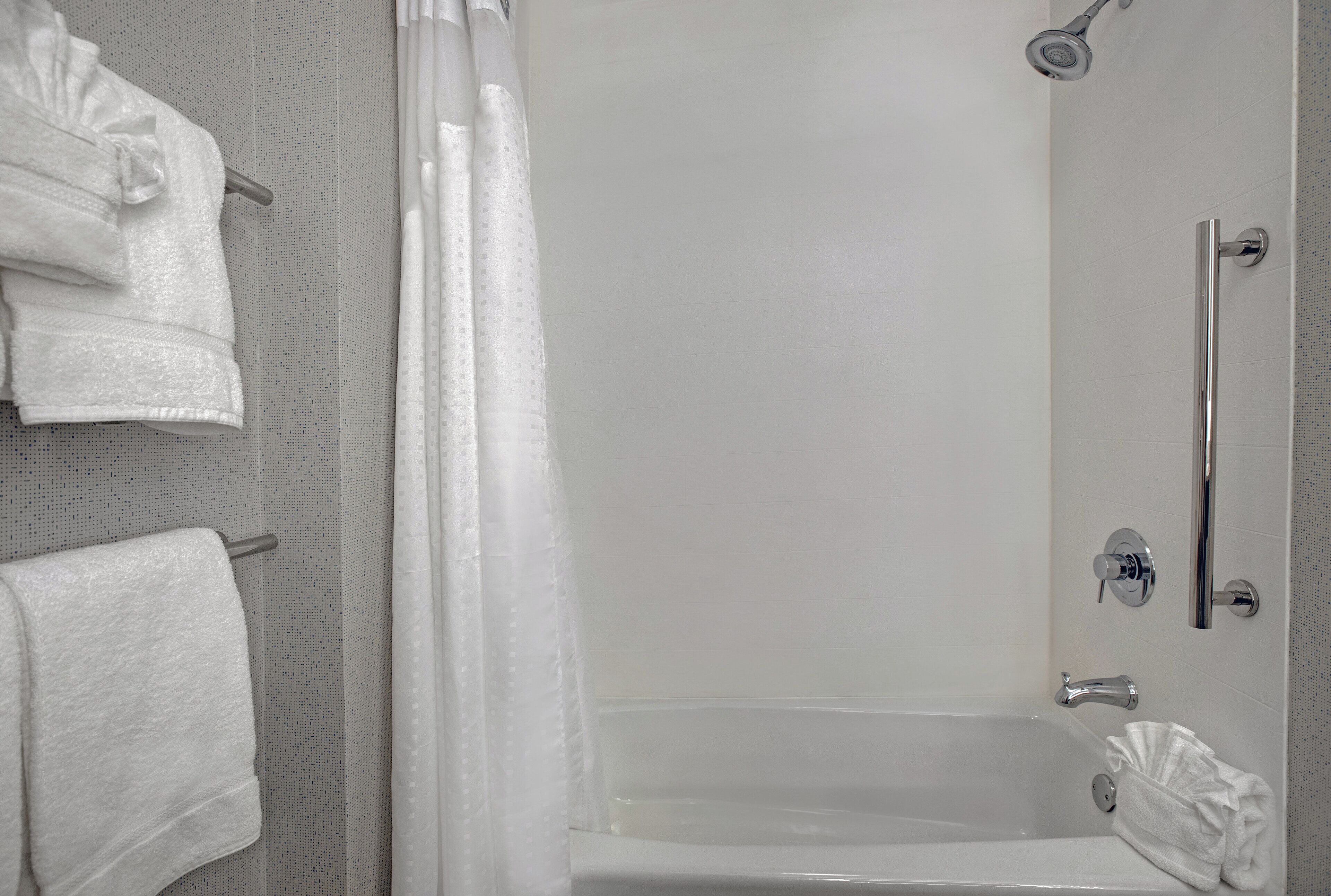 A bathroom with a shower, a bathtub, and a towel rack with towels.