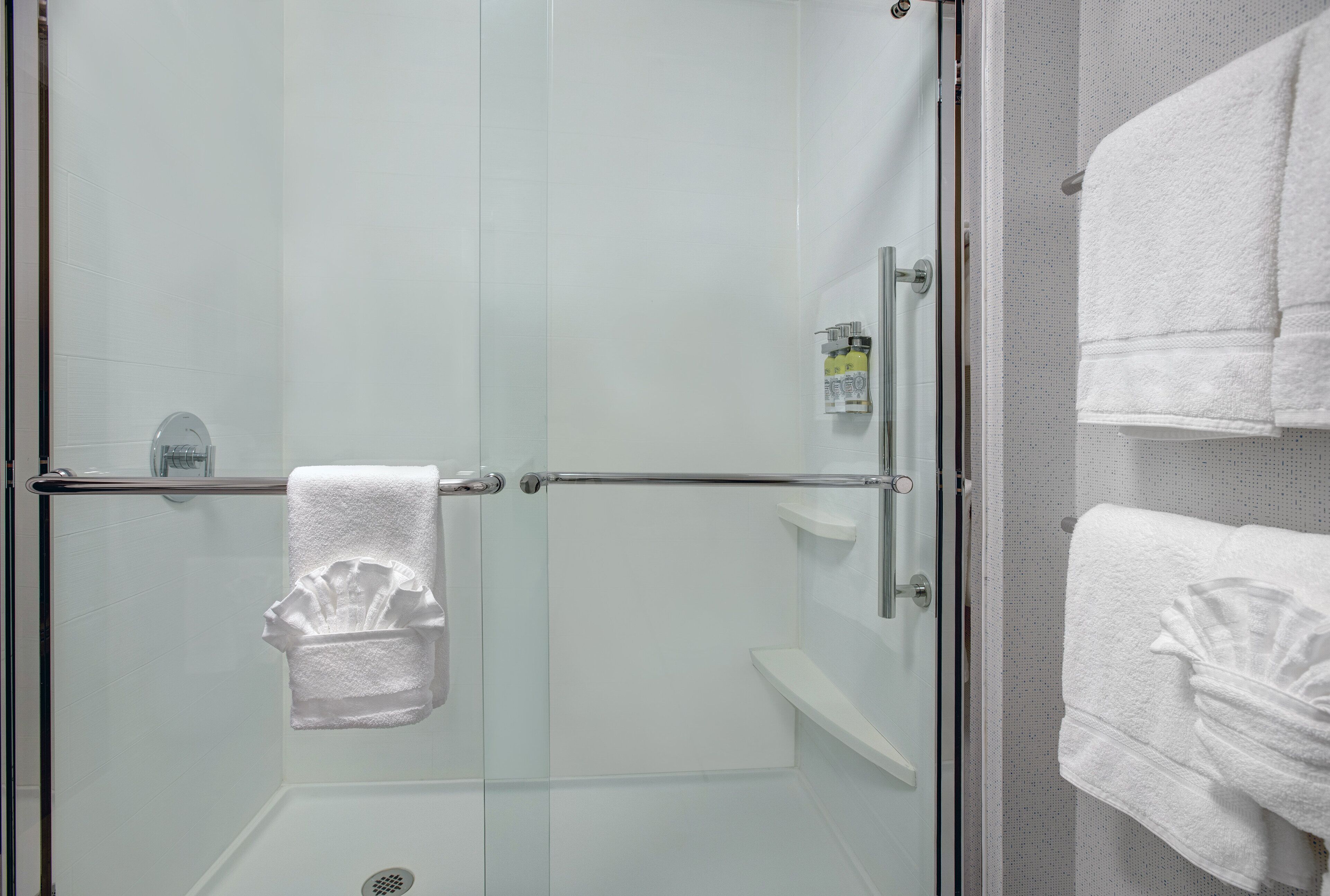 A glass-enclosed shower area with a towel rack and a small shelf with toiletries.