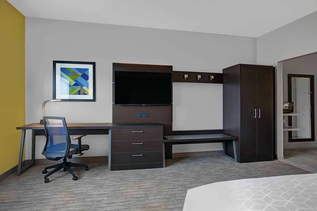 A modern hotel room with a desk, chair, TV, wardrobe, and a bed.