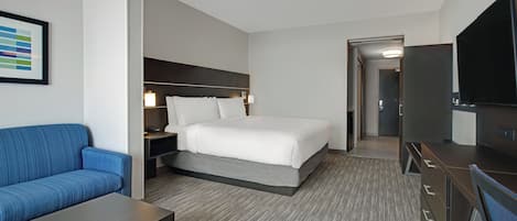 Una habitación de hotel con cama, sofá, escritorio, televisor y puerta que da a otra estancia.